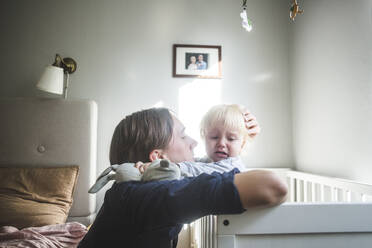 Vater tröstet weinendes blondes Baby in Krippe mit zärtlicher Liebe zu Hause - MASF16389