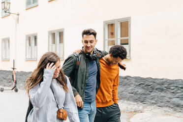 Lächelnde Frau geht mit männlichen Freunden auf der Straße vor einem Gebäude in der Stadt spazieren - MASF16405
