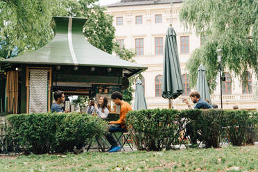 Lächelnde Freunde, die am Imbissstand bei Pflanzen in der Stadt sitzen - MASF16410