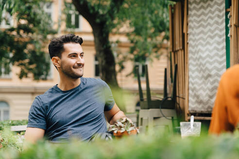 Lächelnder junger Mann sitzt mit einem Freund in einem Restaurant in der Stadt - MASF16411