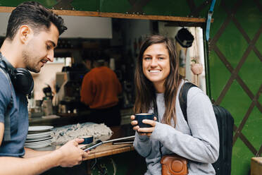 Portrait of smiling woman sitting with male friend by concession stand in city - MASF16413