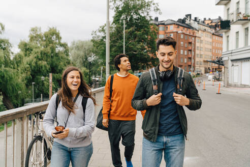 Lächelnde Freunde, die auf der Straße spazieren gehen, während sie die Stadt im Urlaub erkunden - MASF16423