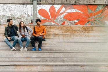 Lächelnde Freunde in voller Länge auf den Stufen sitzend im Urlaub in der Stadt - MASF16424