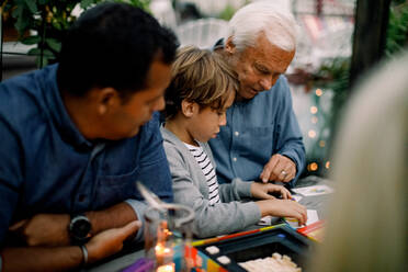 Family playing board game while sitting at table in backyard - MASF16451