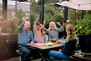 Fröhliche Familie spielt ein Brettspiel, während sie am Tisch im Garten sitzt - MASF16461
