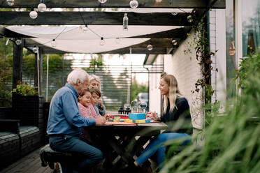 Smiling family playing board game while sitting at table in patio - MASF16463