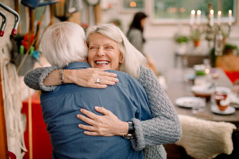 Glückliche ältere Frau, die einen Mann umarmt, während sie zu Hause steht - MASF16466