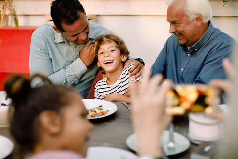 Ältere Frau fotografiert glückliche Familie am Esstisch während des Mittagessens - MASF16468