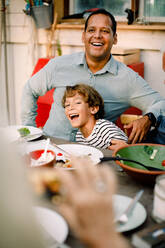 Smiling father and son sitting at dining table during family lunch - MASF16469