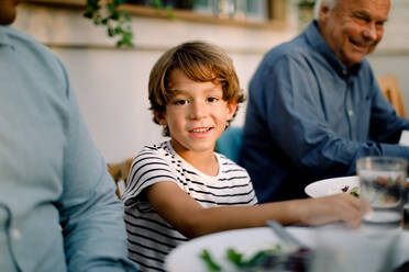 Porträt eines lächelnden Jungen, der mit seiner Familie am Esstisch sitzt, während er zu Mittag isst - MASF16473