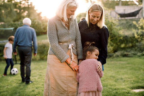 Mädchen umarmt mit Mutter und Großmutter im Hinterhof stehend, lizenzfreies Stockfoto