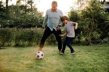 Full length of father and son playing soccer in backyard during weekend activities - MASF16480