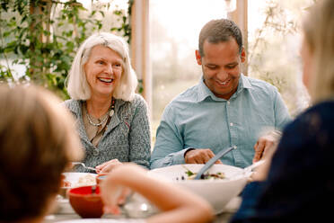 Lächelnde Familie genießt die Mahlzeit am Esstisch beim Mittagessen - MASF16483