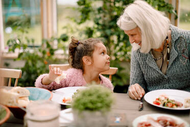 Lächelnde Großmutter sieht ihre Enkelin an, während sie beim Mittagessen am Esstisch sitzt - MASF16484