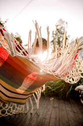 Low angle view of boy sitting in hammock at backyard against sky - MASF16485