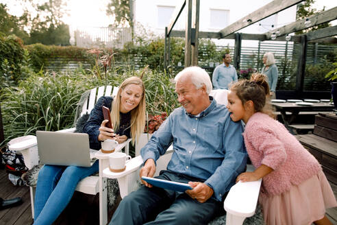 Lächelnde Familie, die am Wochenende im Garten sitzt und digitale Technologie nutzt - MASF16489