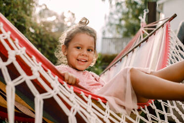 Portrait of playful girl sitting in hammock at backyard - MASF16490