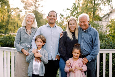 Porträt einer lächelnden Mehrgenerationenfamilie, die an einem Geländer im Hinterhof steht - MASF16493