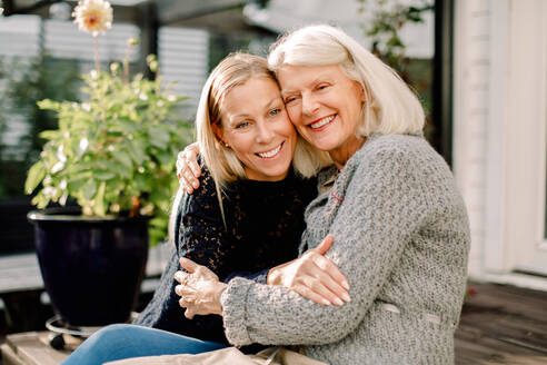 Lächelnde Mutter und Tochter mit Arm um sitzen im Hinterhof - MASF16498