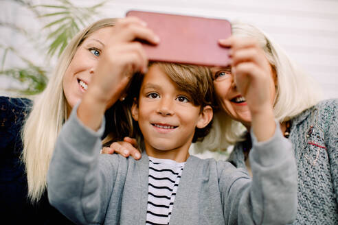 Lächelnder Junge nimmt Selfie mit Mutter und Großmutter in Handy - MASF16504