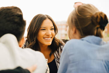 Young female smiling while sitting with friends at social gathering - MASF16525