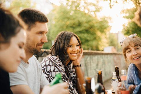 Junge Frau lächelt, während sie mit Freunden bei einem geselligen Beisammensein sitzt - MASF16528