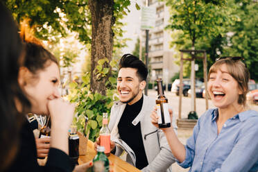 Männliche und weibliche Freunde lachen beim Sitzen mit Getränken auf einer Gartenparty - MASF16546