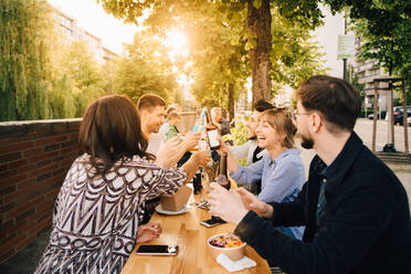 Male and female friends toasting while sitting at social gathering - MASF16550