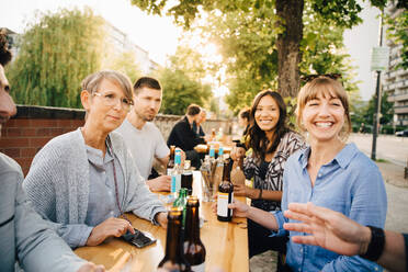 Männliche und weibliche Freunde lachen, während sie mit Getränken am Tisch sitzen - MASF16554