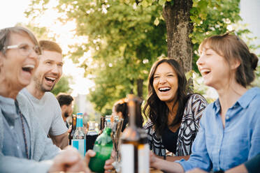 Männliche und weibliche Freunde lachen beim Sitzen mit Getränken im Biergarten - MASF16556