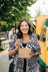 Female customer laughing while standing with box near food truck - MASF16560