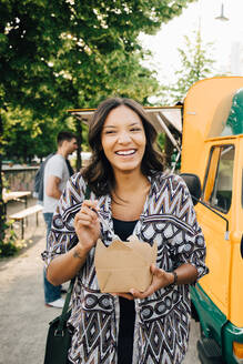 Weiblicher Kunde lacht, während er mit einer Kiste in der Nähe eines Food Trucks steht - MASF16560