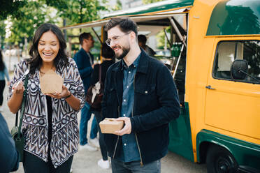 Female laughing while standing by male friend with box against food truck - MASF16562