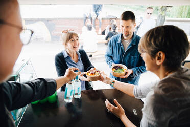 Mature owners serving food and drink to happy customers while standing in commercial land vehicle - MASF16568