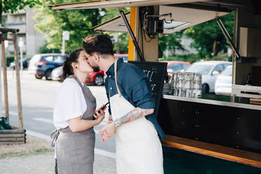 Männliche und weibliche Unternehmer, die sich küssen, während sie an einem Food Truck stehen - MASF16577