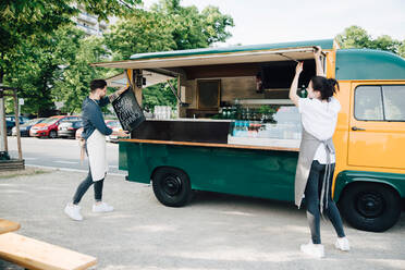 Male owner positioning board on concession stand while female coworker opening shade of food truck - MASF16587