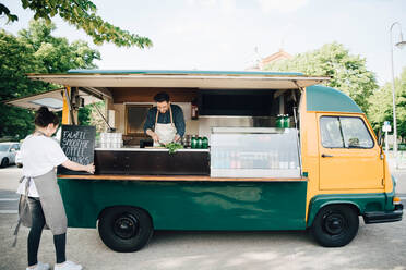 Female owner adjusting board on concession stand while partner working in food truck - MASF16588