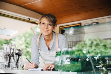 Porträt eines reifen Besitzers, der im Foodtruck stehend die Bestellung aufnimmt - MASF16606