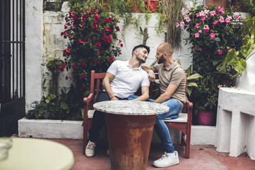 Verliebtes schwules Paar sitzt zusammen auf einer Bank auf einer Terrasse - LJF01243