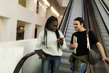 Zwei Studenten mit Mobiltelefon auf einer Rolltreppe - VABF02603