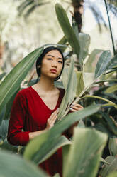 Porträt einer schönen jungen Frau in einem Garten mit großen Blättern - TCEF00113