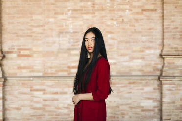 Porträt einer schönen jungen Frau in einem roten Kleid vor einer Backsteinmauer - TCEF00135