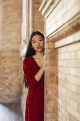 Portait of beautiful young woman wearing a red dress at a brick wall - TCEF00138