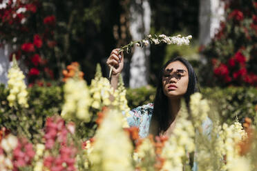 Schöne junge Frau mit Blume in einem öffentlichen Garten im Frühling - TCEF00144