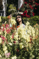 Schöne junge Frau mit Blume in einem öffentlichen Garten im Frühling - TCEF00145