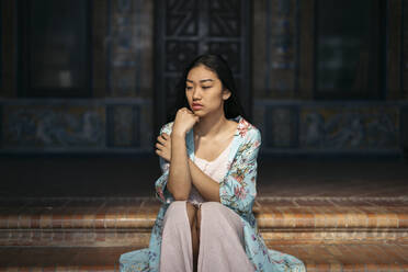 Portait of beautiful young woman sitting on steps wearing a kimono - TCEF00165