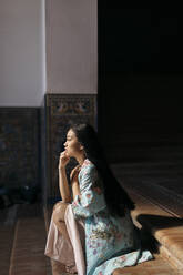 Porträt einer schönen jungen Frau, die auf einer Treppe sitzt und einen Kimono trägt - TCEF00167