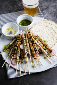Skewers of meat on plate with yogurt and parsley sauce with flat bread and vegetables - GIOF07957