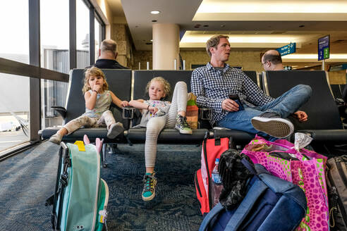 Zwei Mädchen und Vater sitzen Nase bohren warten im Flughafen - CAVF74287