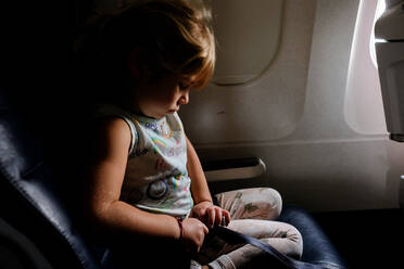 Little girl putting on airplane seatbelt in dramatic light - CAVF74292